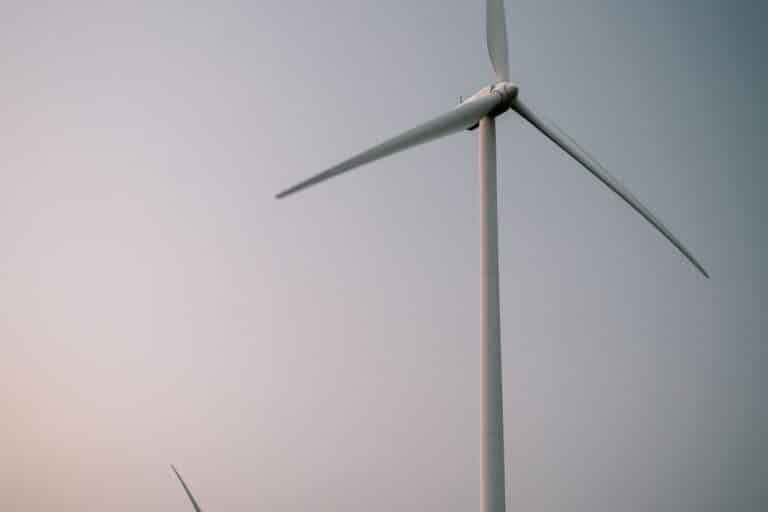 Tři vysoké větrné elektrárny s bílými vrtulemi stojí v otevřeném poli pod oblohou