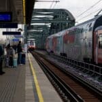 Cestující stojí na nástupišti nádraží a čekají na přijíždějící vlak