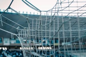 Detail fotbalové branky se sítí, v pozadí tribuna stadionu