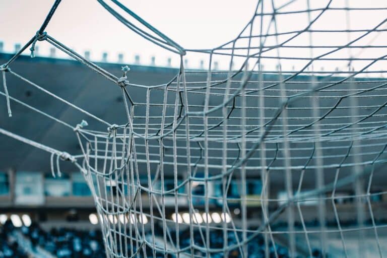 Detail fotbalové branky se sítí, v pozadí tribuna stadionu