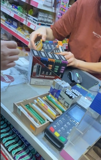 Prodavač podává balení jednorázových elektronických cigaret přes pult obchodu