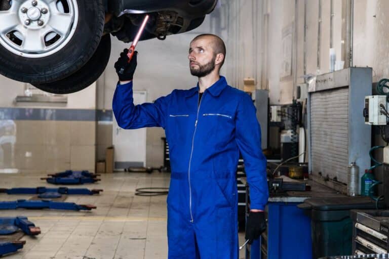 Automechanik v modré kombinéze prohlíží otevřenou kapotu osobního auta v dílně autoservisu