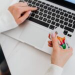 Ruce drží platební kartu před otevřeným notebookem při nákupu na internetu