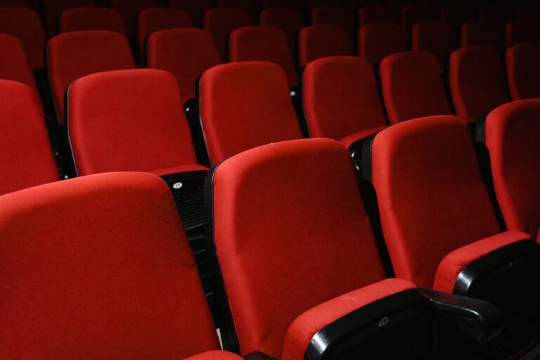 Prázdná řada červených sedadel v potemnělém kinosále s promítacím plátnem