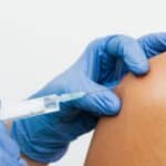 Zdravotník v rukavicích aplikuje injekční stříkačkou vakcínu do paže pacienta