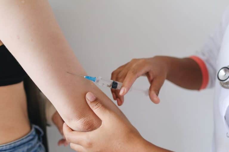 Zdravotník v rukavicích aplikuje injekci do paže pacienta
