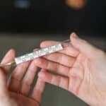 Ruce drží lékařský teploměr, osoba je zabalená v dece