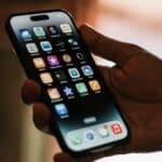 Detail ruky držící chytrý telefon, na displeji jsou zaostřené ikony aplikací
