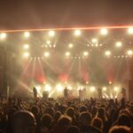 Rocková kapela hraje na pódiu osvětleném barevnými reflektory před večerním publikem.