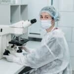 Laborant v ochranném obleku a respirátoru pracuje u mikroskopu ve sterilní laboratoři
