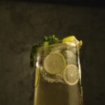 Sklenice limonády s ledem, plátky limetky a bazalkou na tmavém pozadí