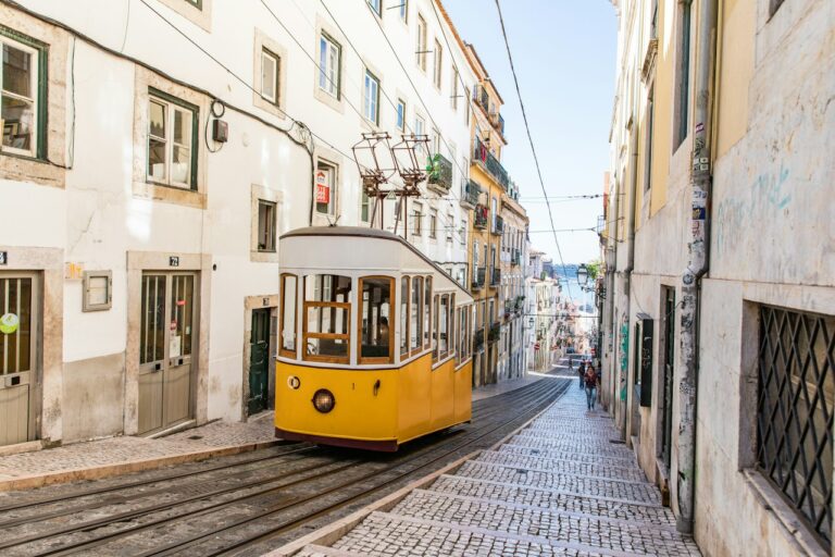 Žlutobílá tramvaj projíždí ulicí Lisabonu za denního světla
