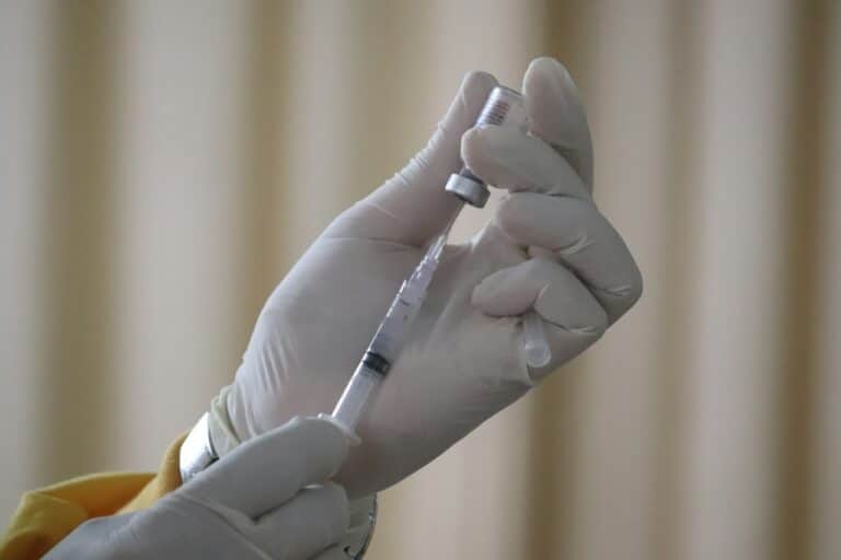Ruce v bílých latexových rukavicích natahují tekutinu z lahvičky do injekční stříkačky