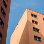 Fasády dvou panelových domů s okny proti modré obloze
