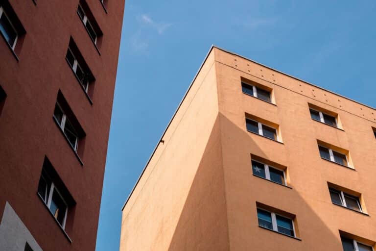Fasády dvou panelových domů s okny proti modré obloze