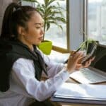 Mladá žena sedí u pracovního stolu, drží kalkulačku a prochází papírové doklady
