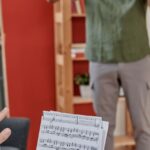 Mladý houslista hraje v místnosti, vedle něj stojí učitel s notami v ruce