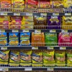 Regál v supermarketu plný barevně balených snacků a trvanlivých potravin