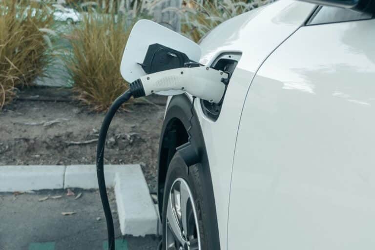 Bílý elektromobil stojí na parkovišti připojený kabelem k nabíjecí stanici