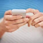 Detail ženských rukou s prsteny, které drží chytrý telefon a píší na něm zprávu