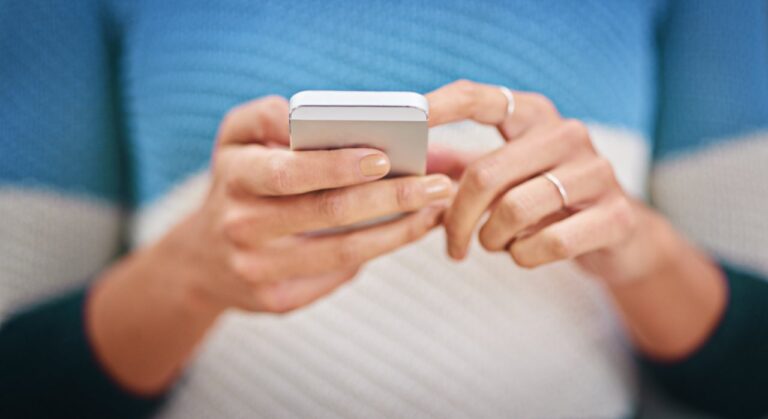 Detail ženských rukou s prsteny, které drží chytrý telefon a píší na něm zprávu